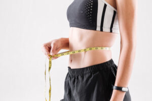 Femme sportive mince mesurant sa taille avec un mètre ruban jaune, fond blanc.
